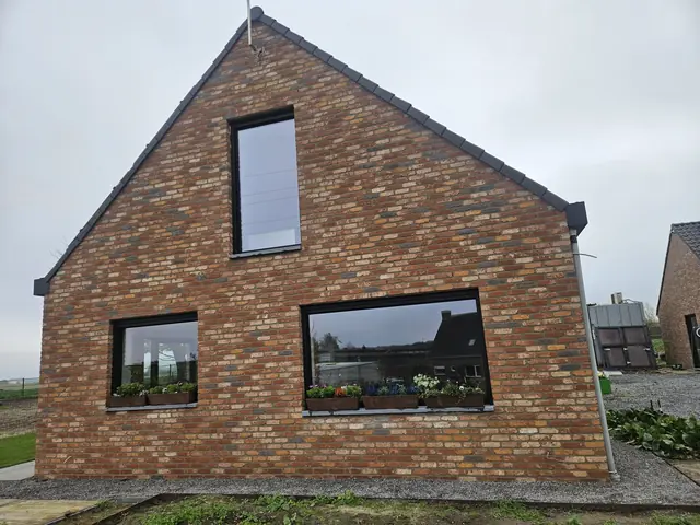 Puntgevel in rode baksteen met moderne zwarte ramen