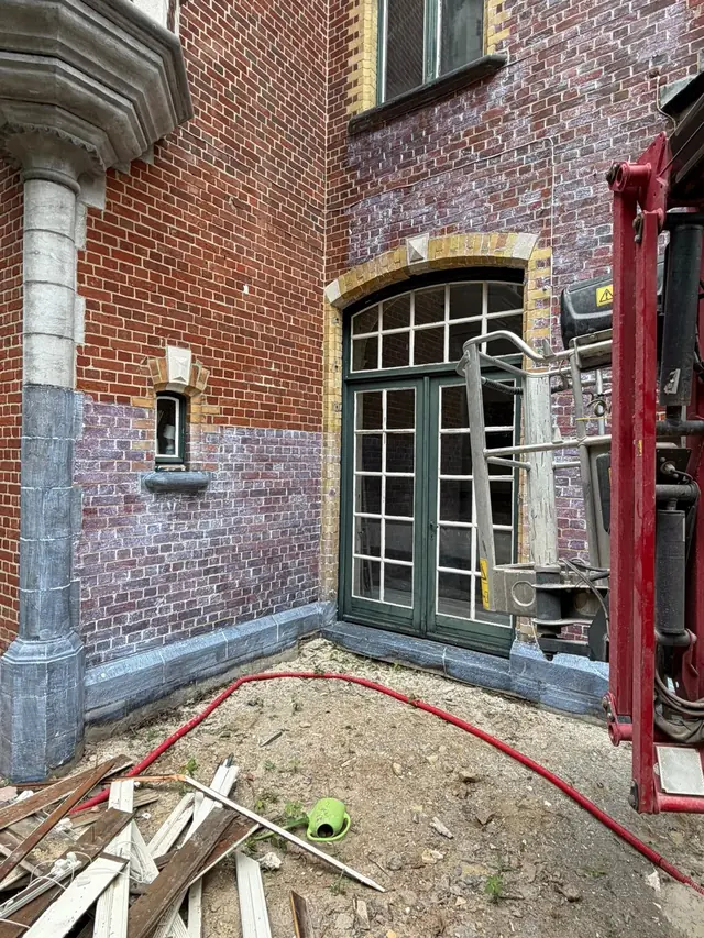 Hoek van dezelfde gevel: onderaan nog grijze aanslag, bovenaan gereinigde rode baksteen