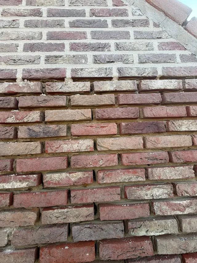 Gevel halverwege het hervoegen: bovenaan nieuwe voegen, onderaan nog de oude