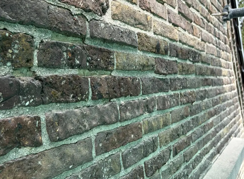 Bakstenen gevel in Kortrijk met verweerde voegen en groene aanslag, vóór de renovatie