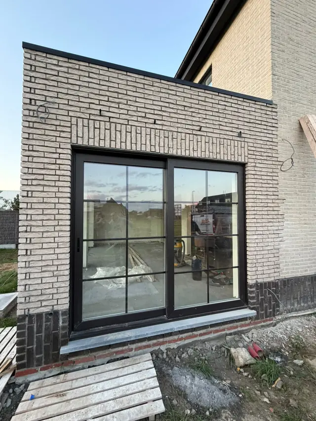 Aanbouw in lichte baksteen met zwarte schuiframen in Lauwe na het voegen